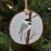 A handmade wood slice Christmas ornament with an acrylic painting of a chickadee in the snow at Cove Creek Photography.